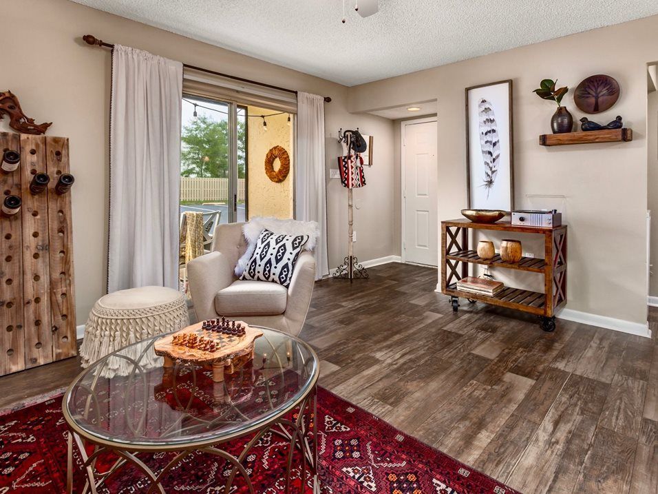 Living room with a glass-top coffee table, armchair, rug, wine rack, and sliding glass door to a patio.