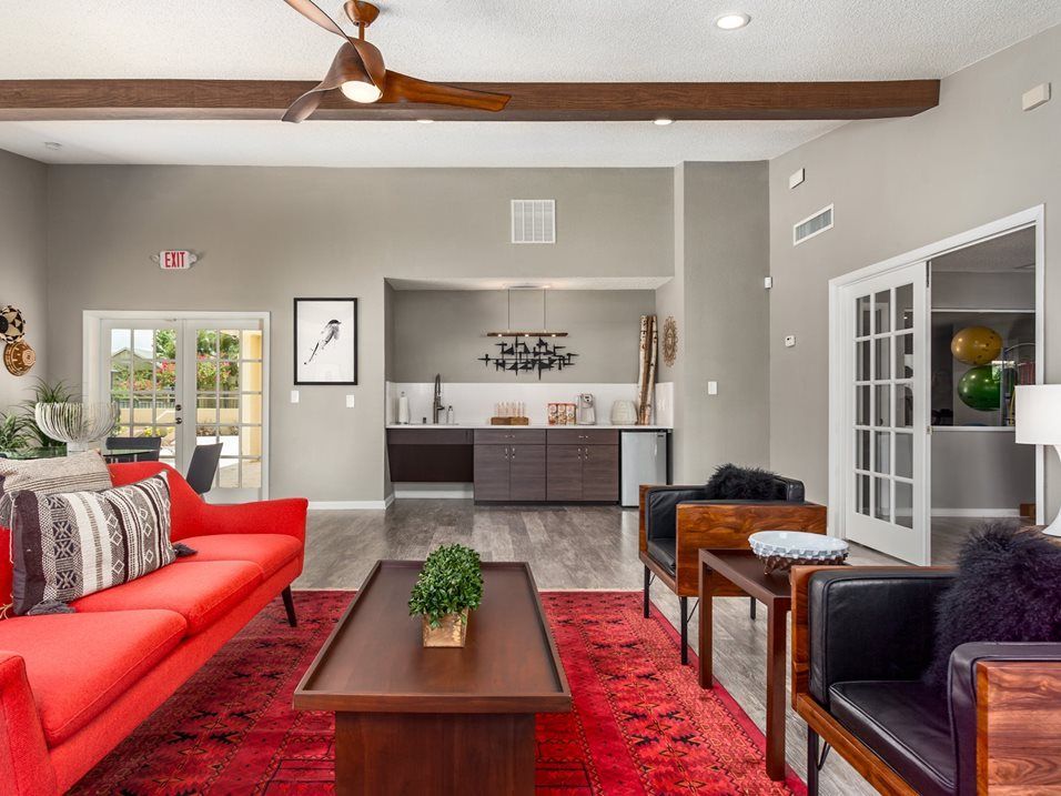 Spacious living room with red sofa, rug, and dark wood furniture. Kitchenette in background.