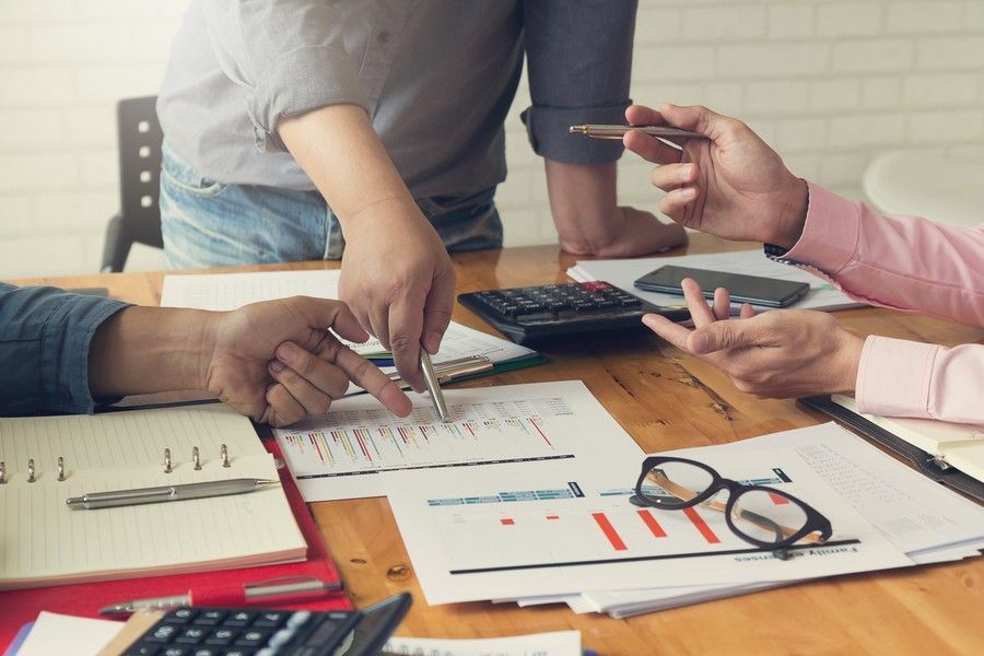 People at a wooden table reviewing papers with charts, graphs, and calculators. One person points at a document.