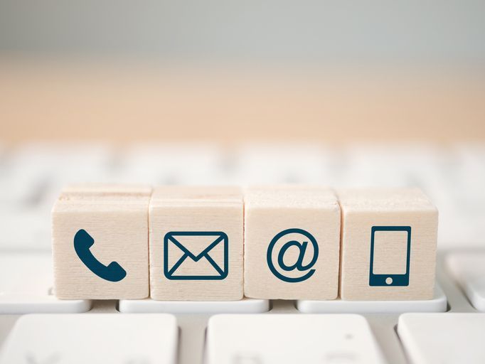Wooden blocks with phone, email, email address, and mobile phone icons, arranged on a keyboard, suggesting contact options.