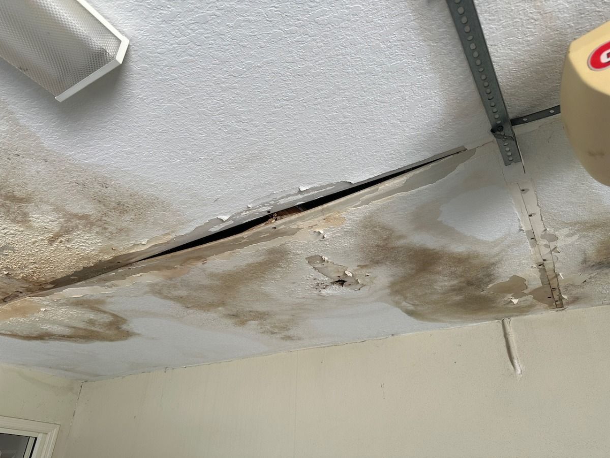A water-damaged garage ceiling with large brown stains, peeling paint, and a deep, structural crack.