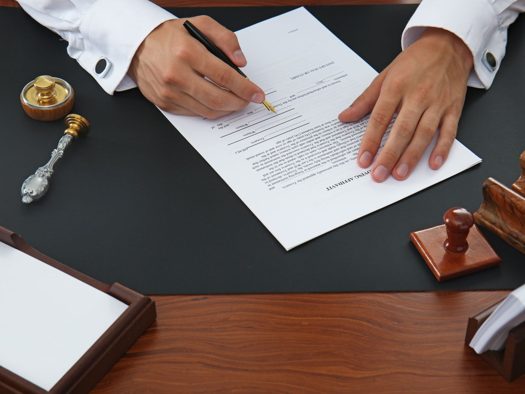 Person signing a document at a desk, with ink, stamps, and a paper tray.
