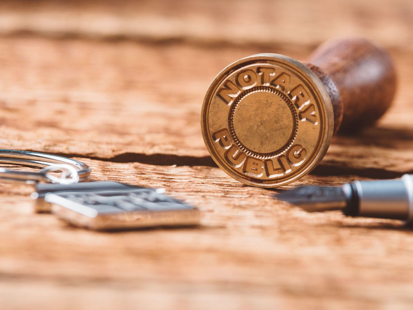 Gold notary public stamp on a wooden surface, with a pen and keys nearby.