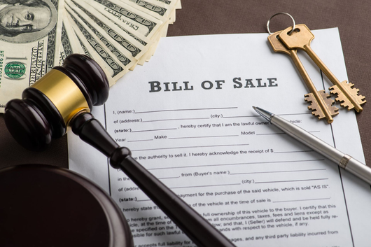 Bill of sale with gavel, money, keys, and pen on a desk, indicating a legal or financial transaction.