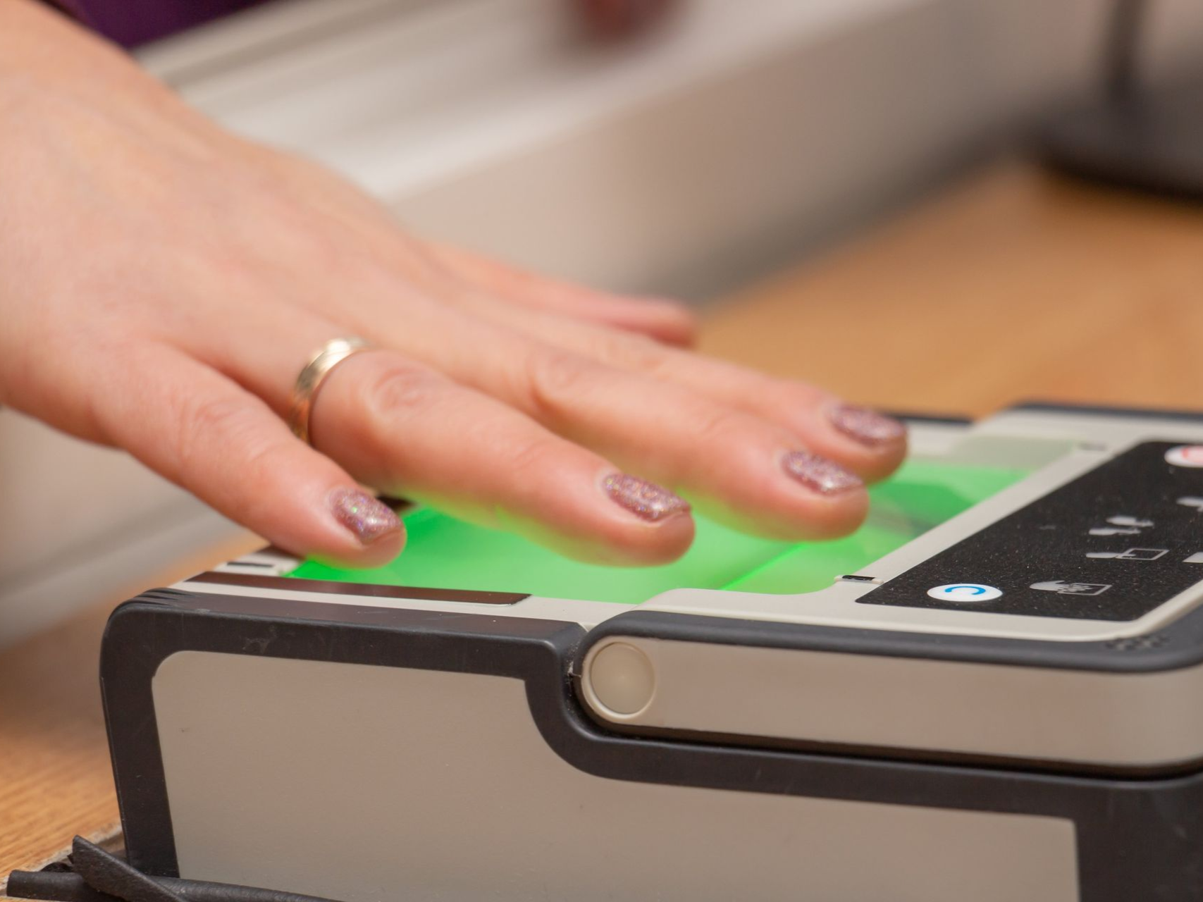 Hand scanning fingerprint on a biometric scanner, with green light visible.