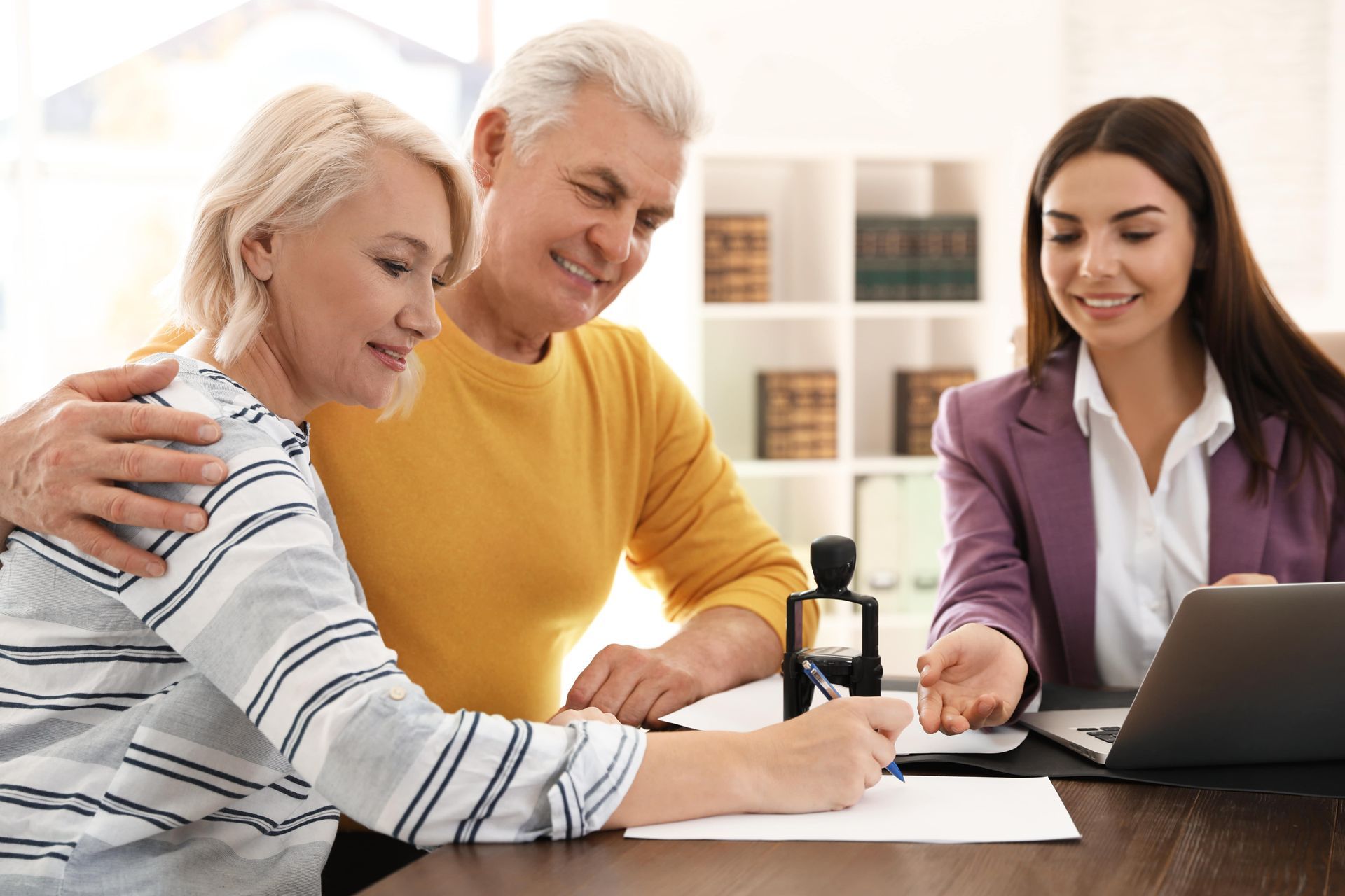 Senior couple signing documents with a smiling advisor at a desk.
