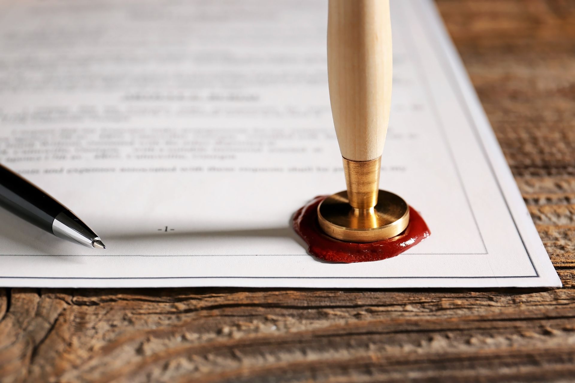 Seal pressed into red wax on a document, next to a pen, all on a wooden surface.