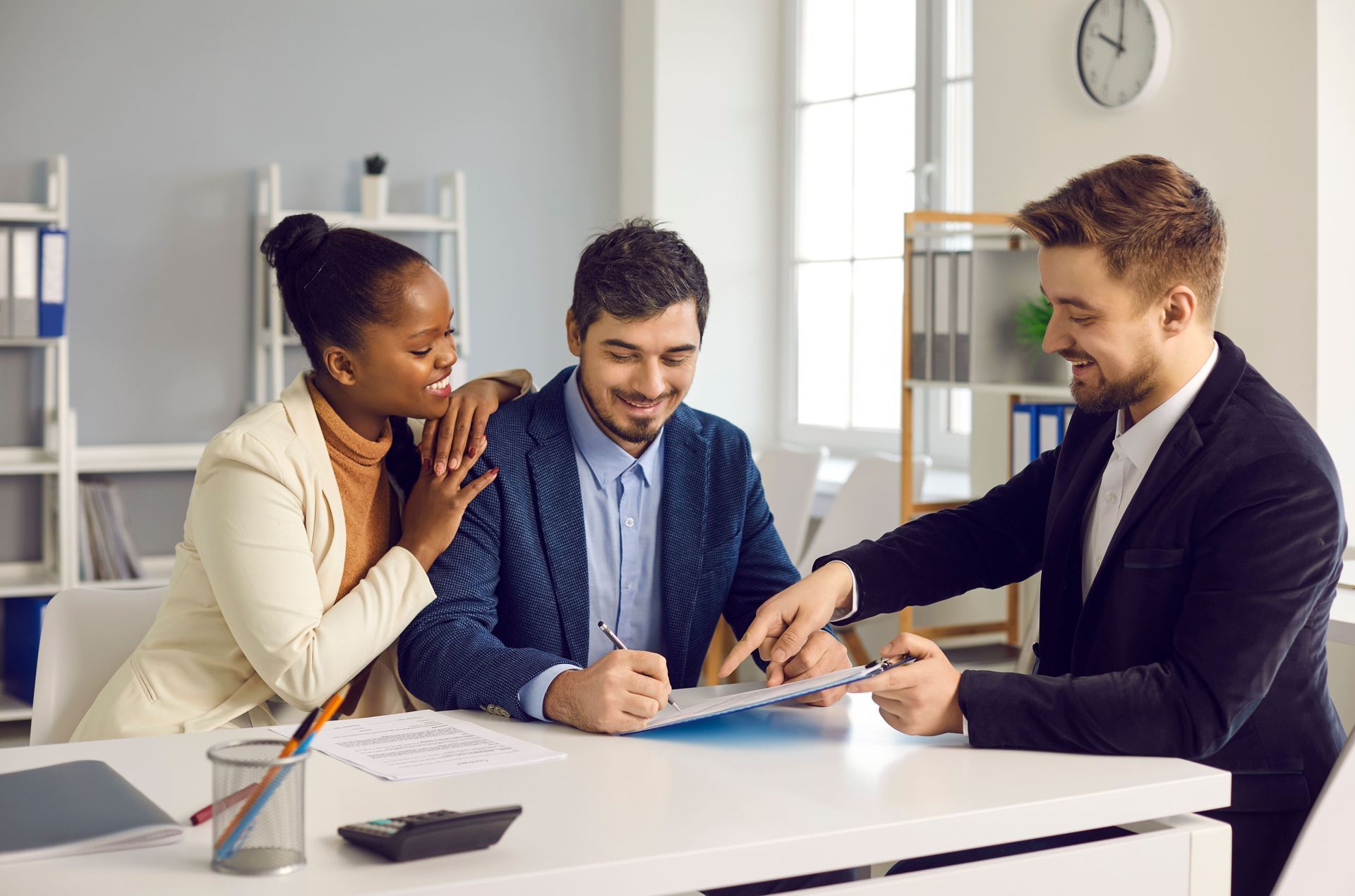 Couple signing document at a desk with a smiling advisor in an office setting.