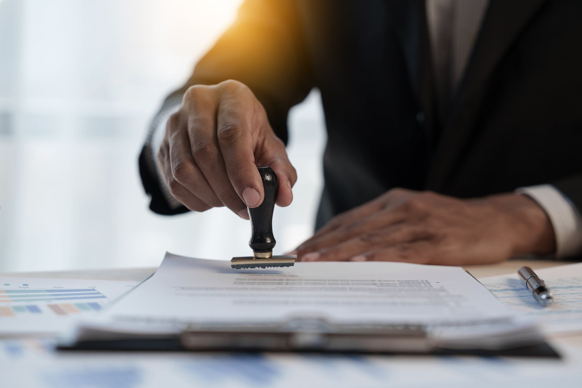 Person in suit stamping a document on a desk. Sunlight highlights the scene.