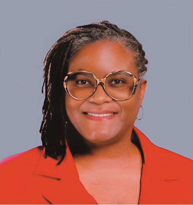 Woman with glasses, dreadlocks, wearing a red jacket, smiling.