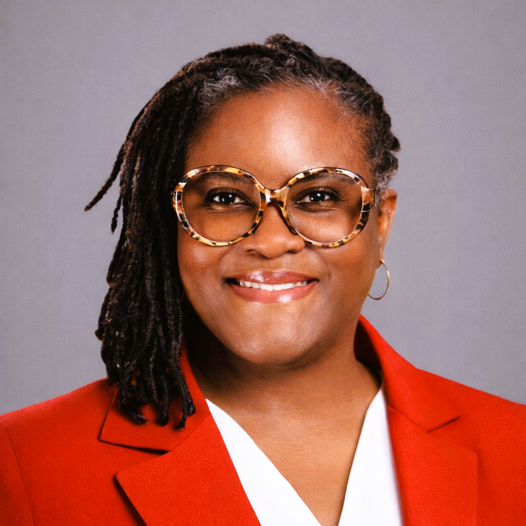 Woman with glasses, dreadlocks, wearing a red jacket, smiling.