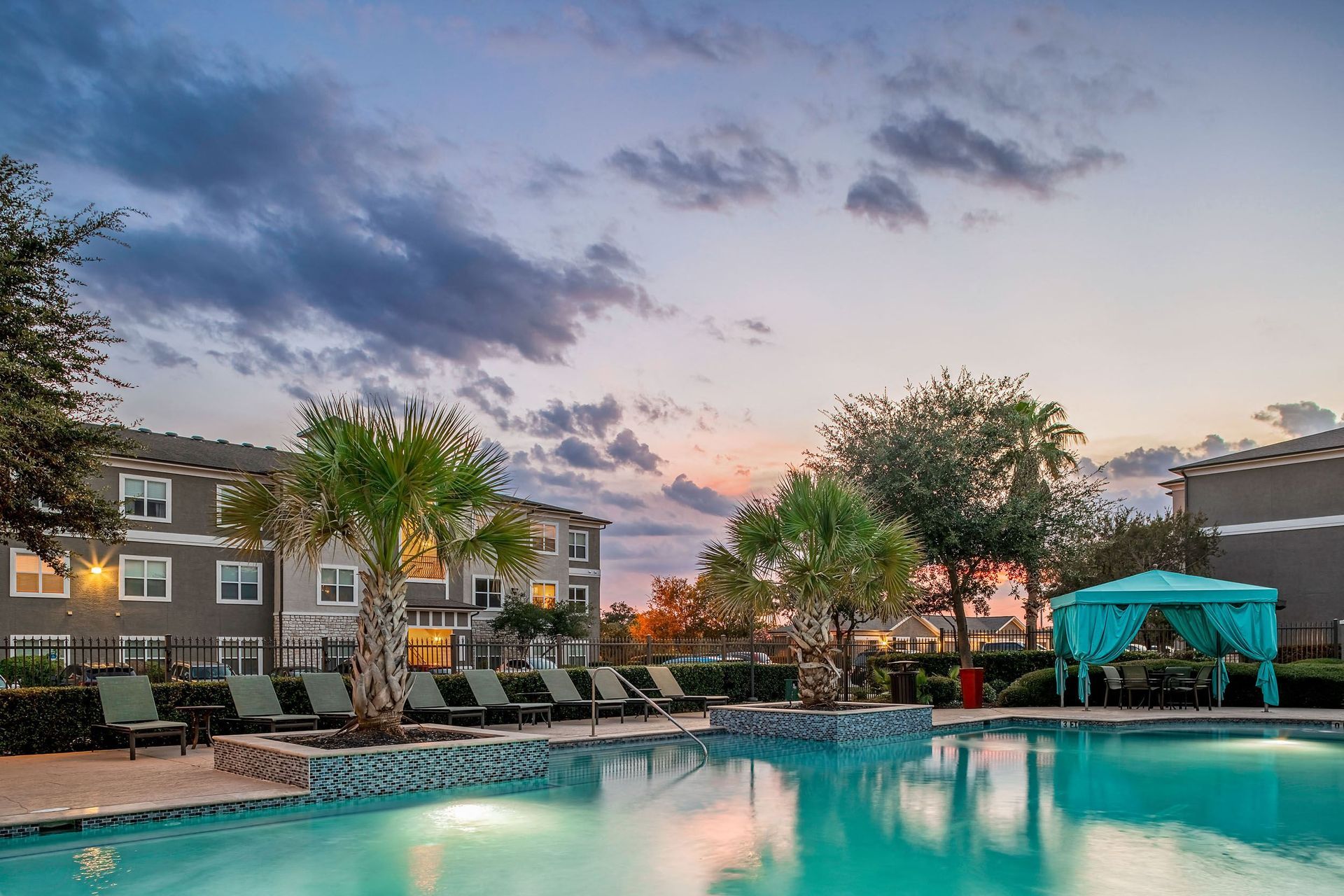 a swimming pool with chaise lounge chairs and palm trees with an apartment building in the background