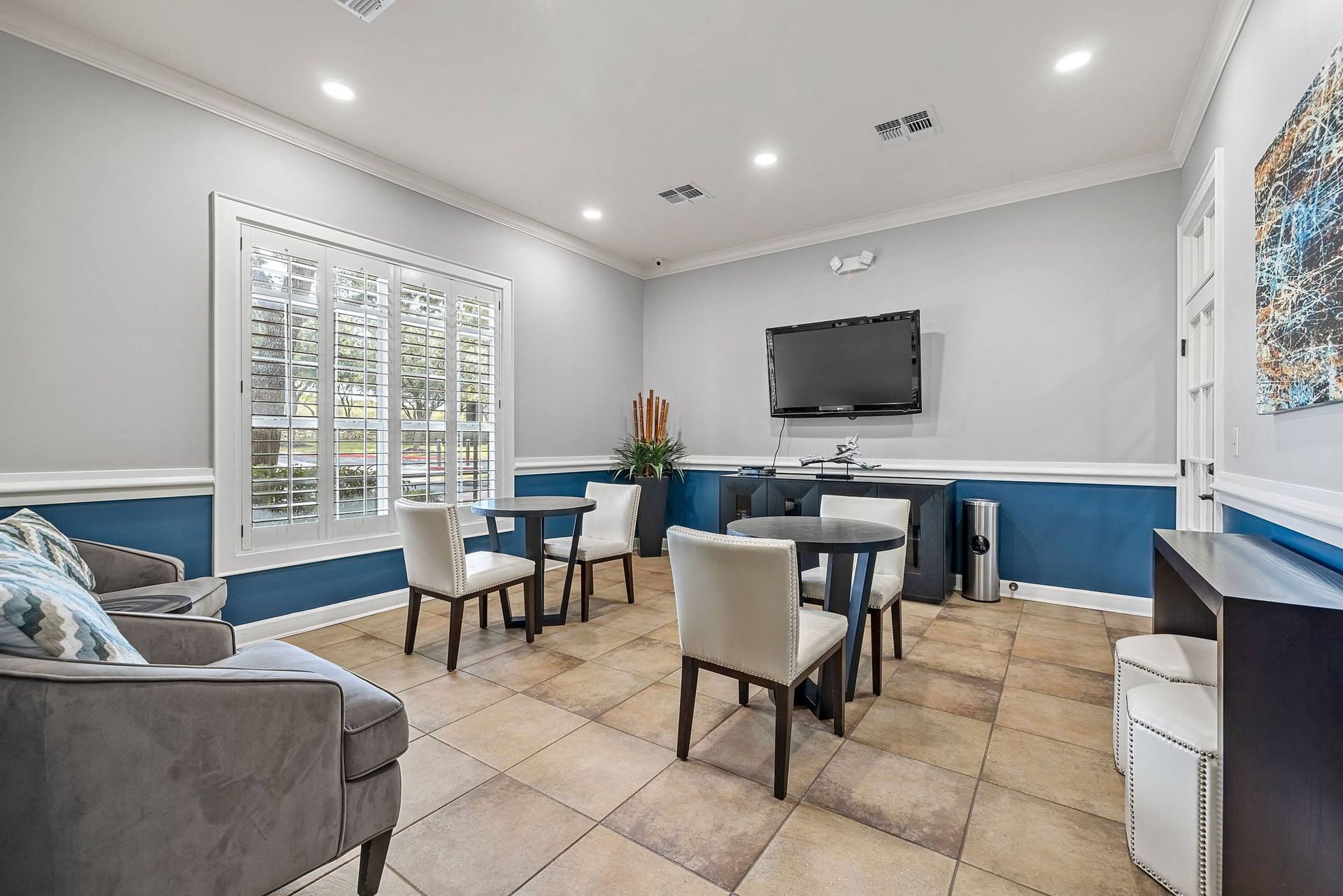 a lounge area with chairs and tables and a television on the wall