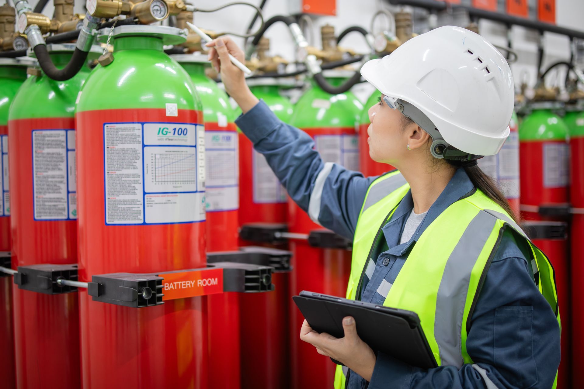 Person in hard hat and safety vest inspecting fire suppression cylinders.