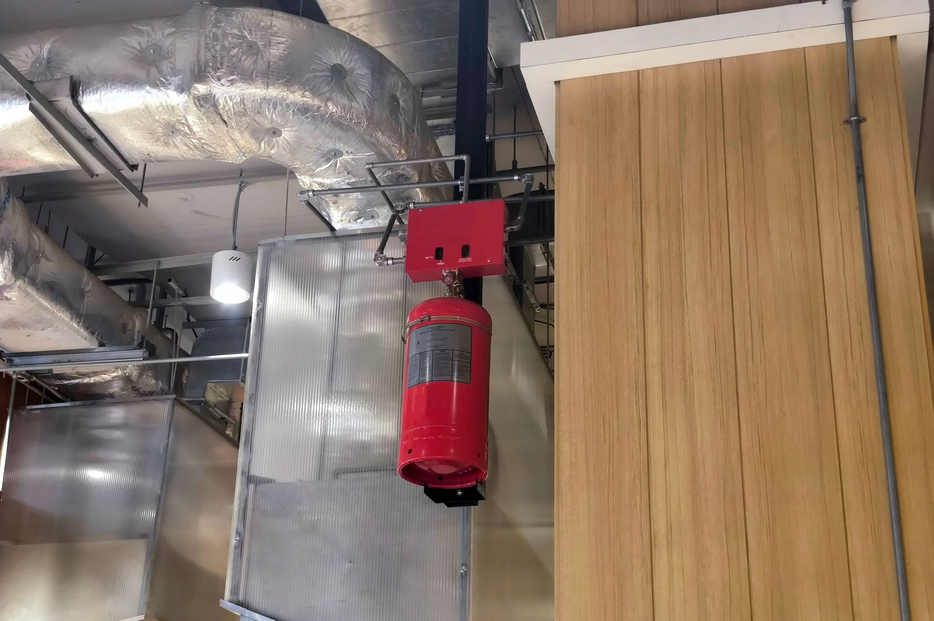 Red fire extinguisher hanging from ceiling next to a wooden panel.