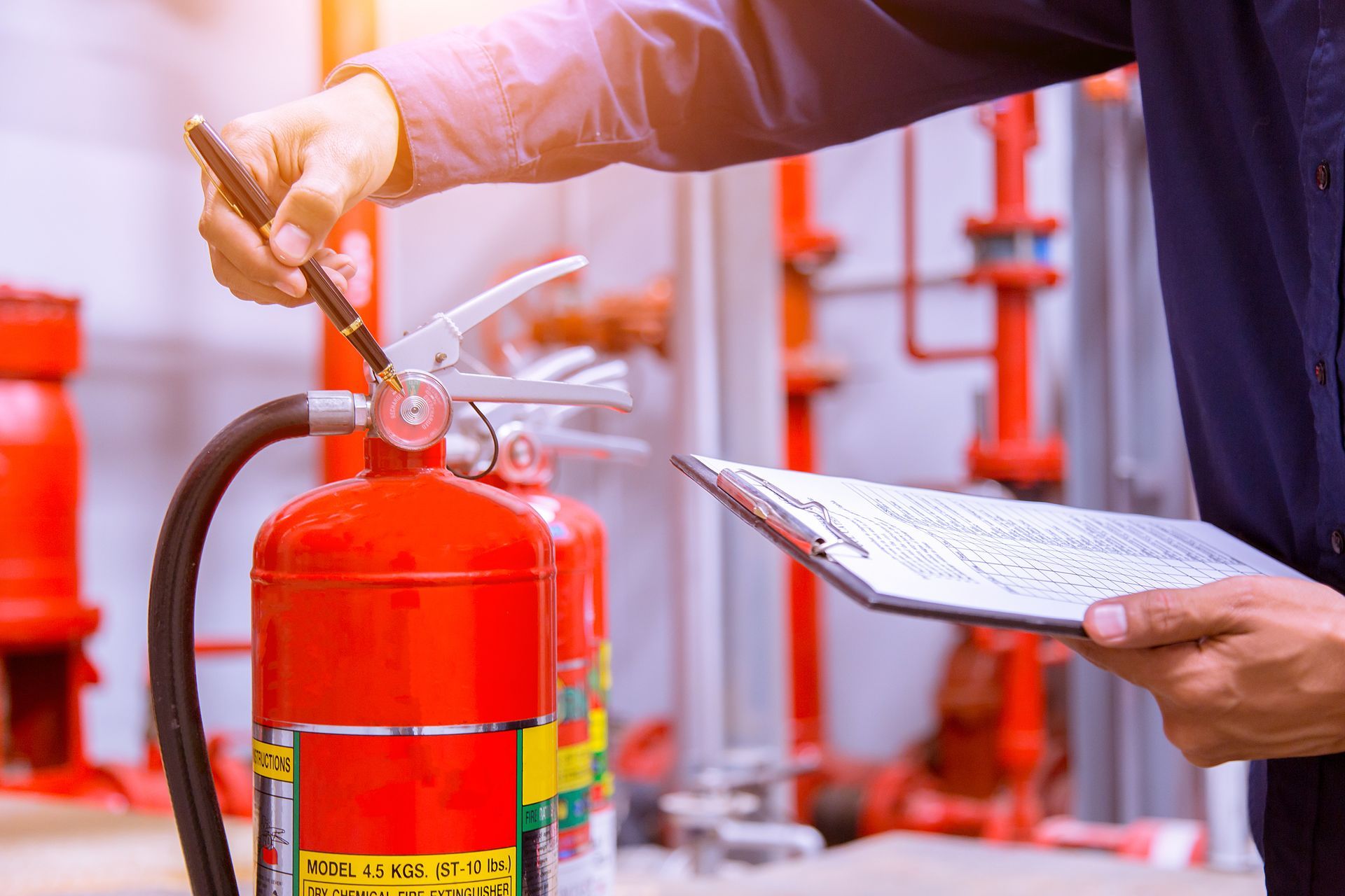 Person inspecting a red fire extinguisher in a building, using a clipboard and pen.