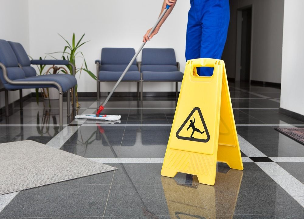 A Person Is Mopping The Floor Next To A Yellow Caution Sign — Sadie's Cleaning Services in Yeppoon, QLD