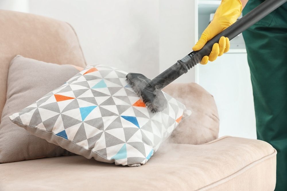 A Person Is Cleaning A Pillow On A Couch With A Steam Cleaner — Sadie's Cleaning Services in Emu Park, QLD