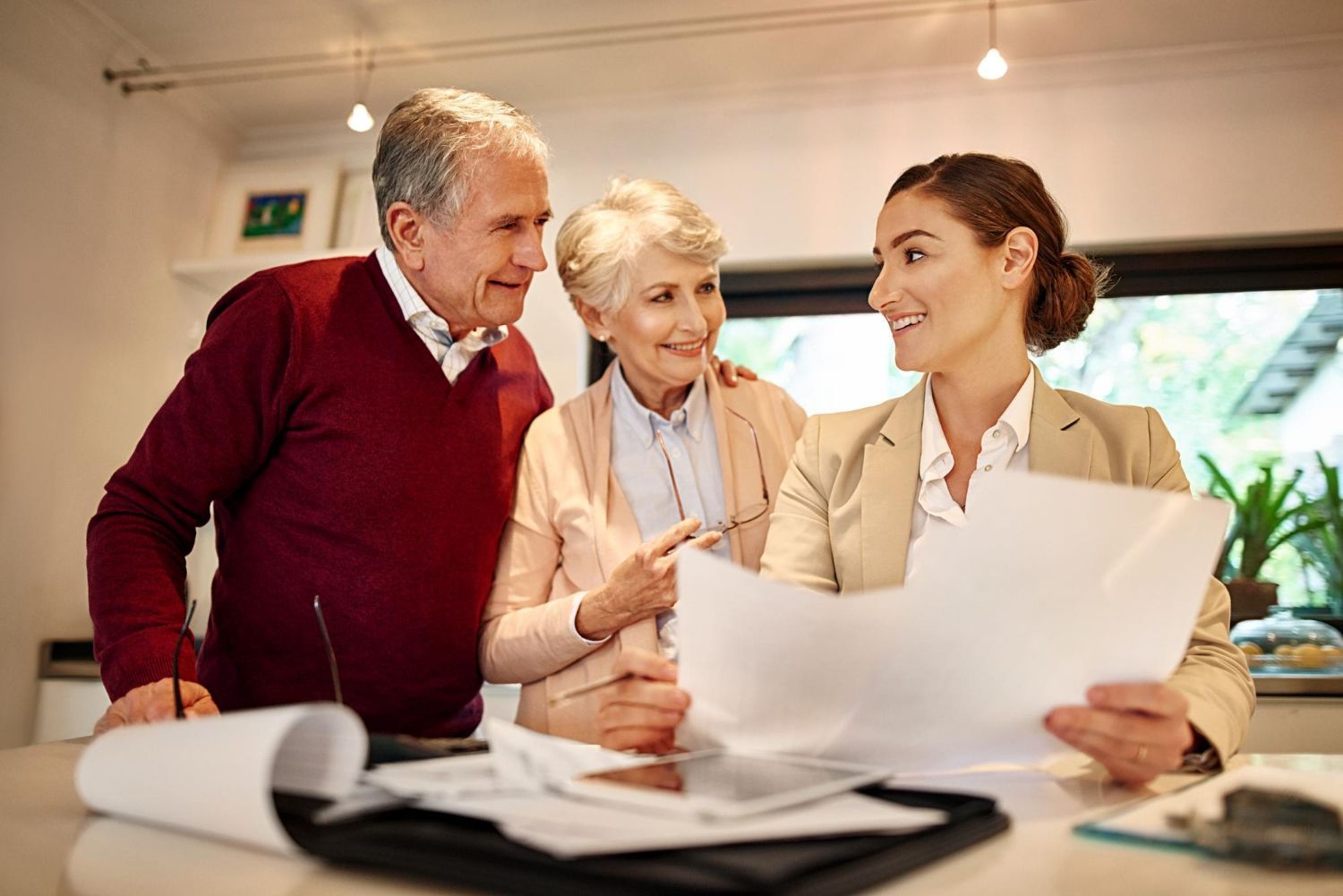 Three people reviewing documents at a desk in a bright office, smiling and discussing plans