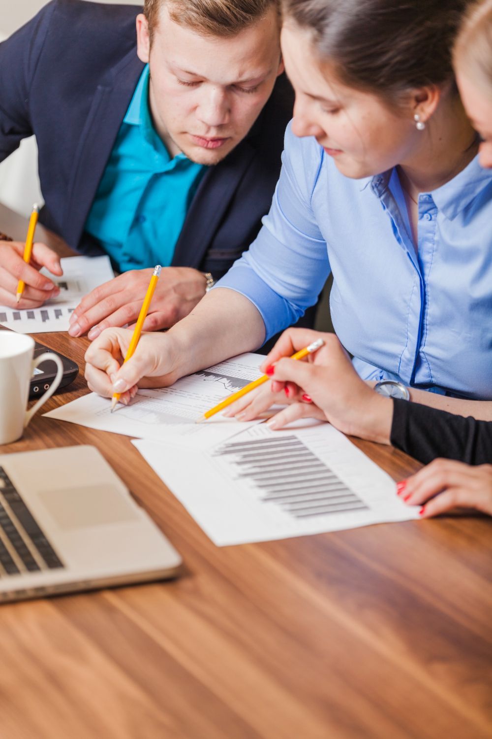 Colleagues reviewing charts and notes at a desk with a laptop and pencils