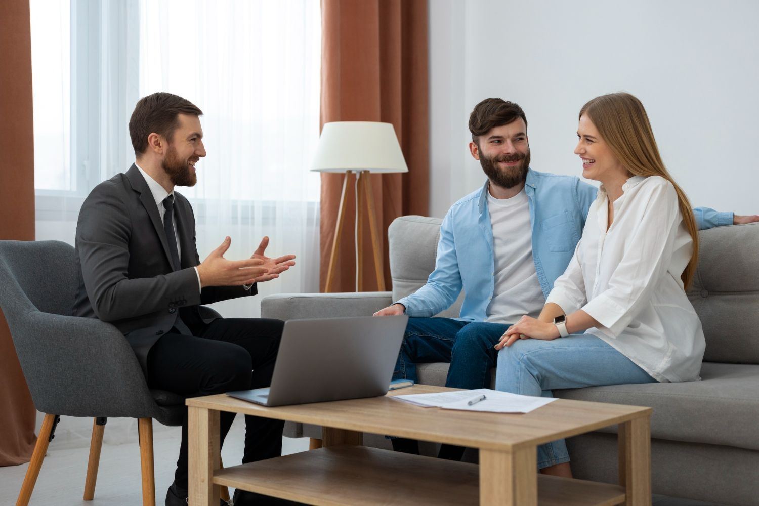 Three people talking in a bright living room with a laptop and coffee table