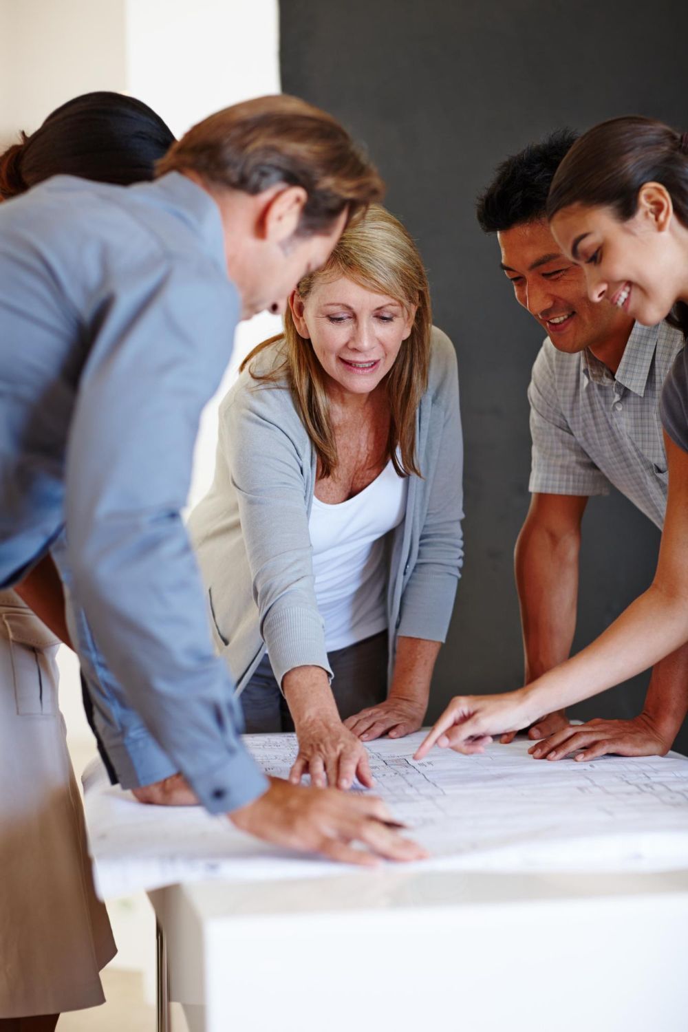 Team collaborating around a table with architectural plans, leaning in and discussing the design.