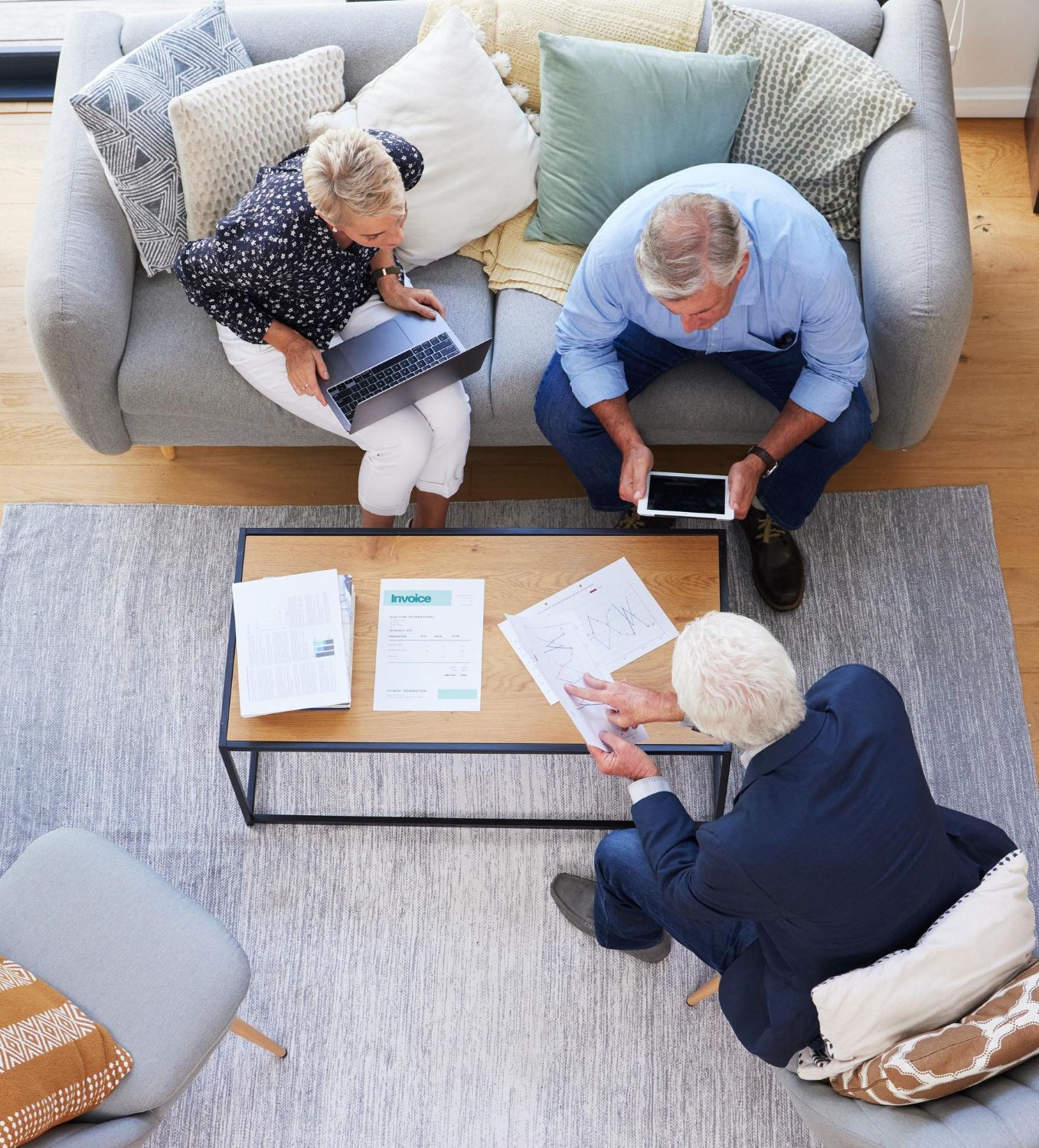 Three people seated around a coffee table, reviewing papers and tablets in a bright living room.