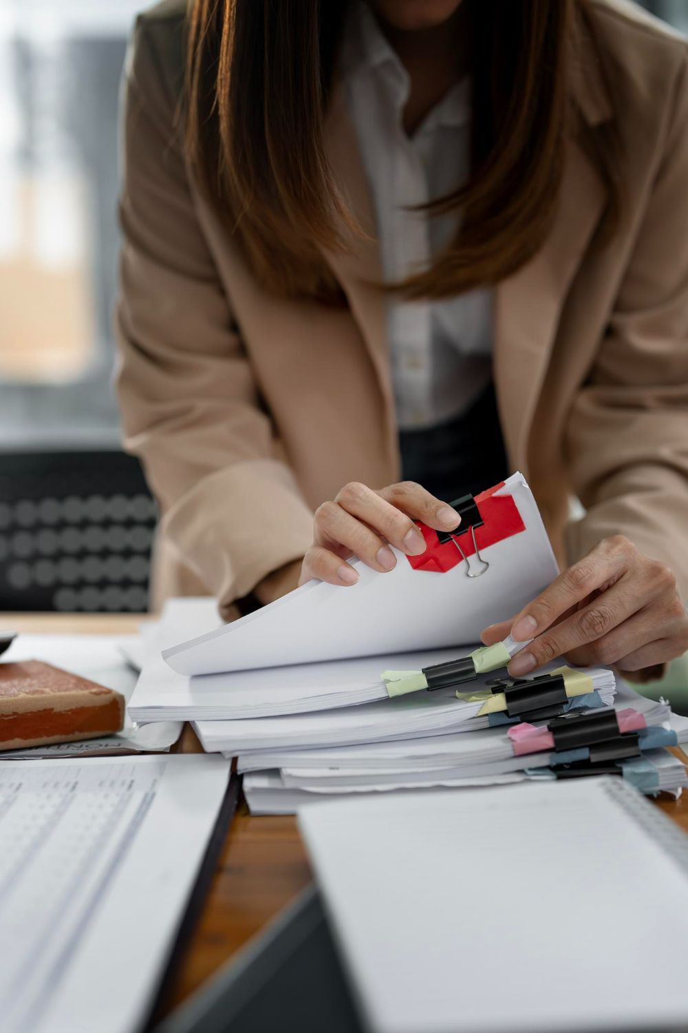 Hands sorting stacked papers and notebooks on a desk in an office setting