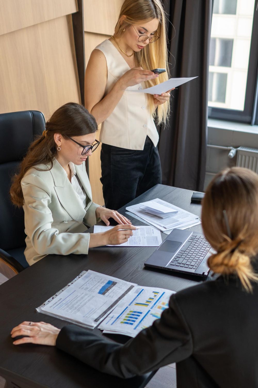 Three coworkers reviewing documents around a laptop in a modern office