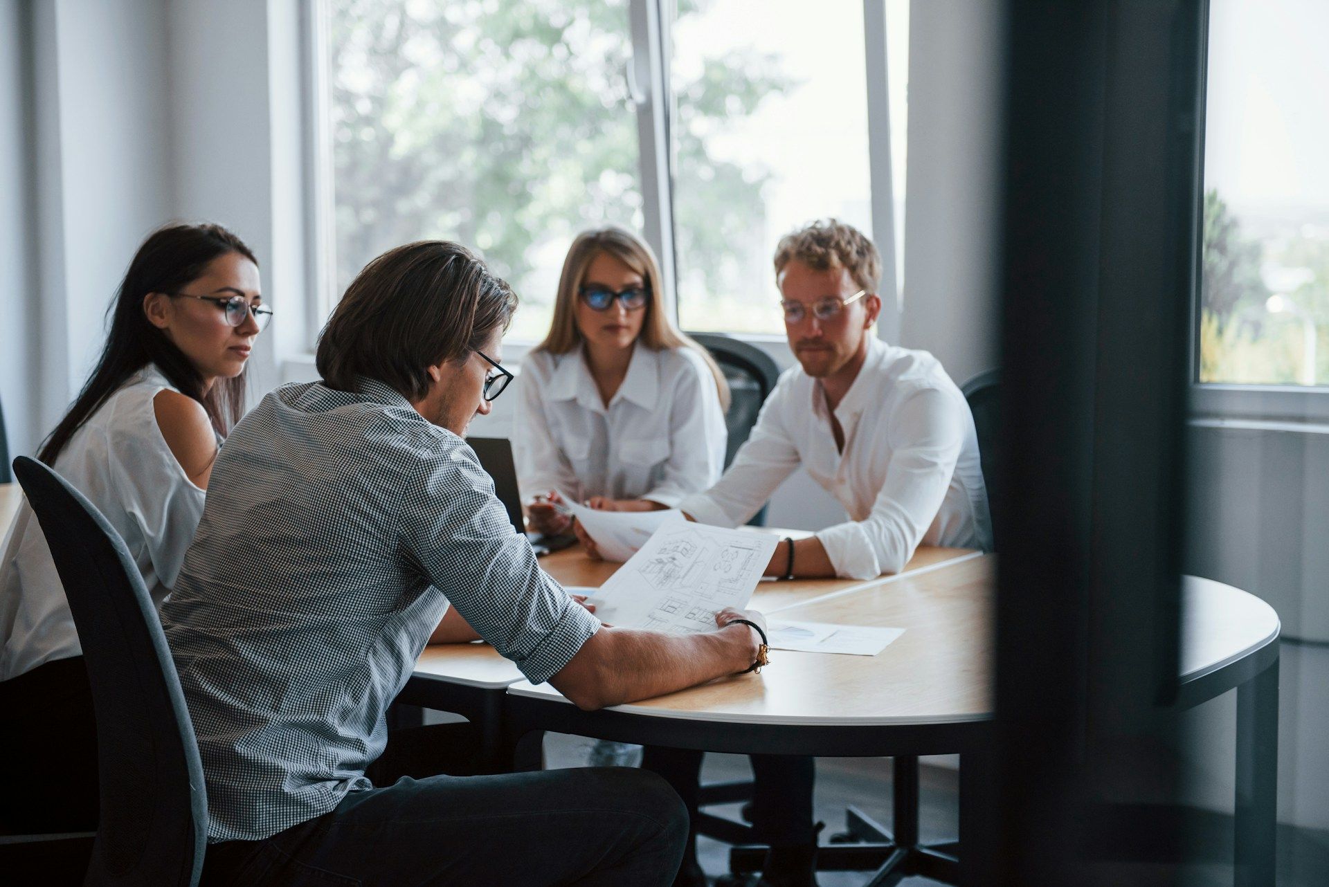 Four coworkers in a meeting around a table, reviewing documents in a bright office.