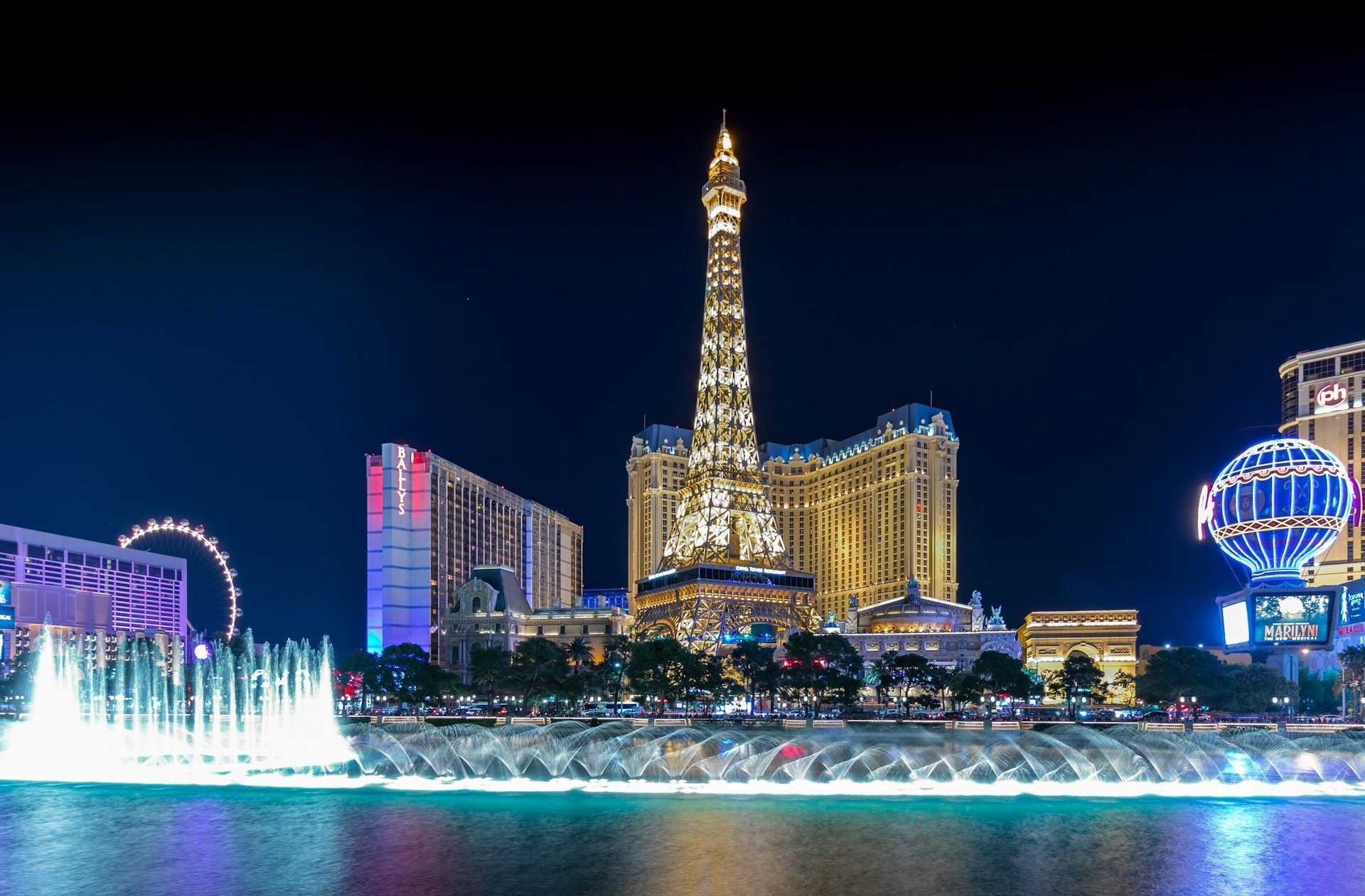 Las Vegas Strip at night with the Eiffel Tower replica lit up and colorful fountain show