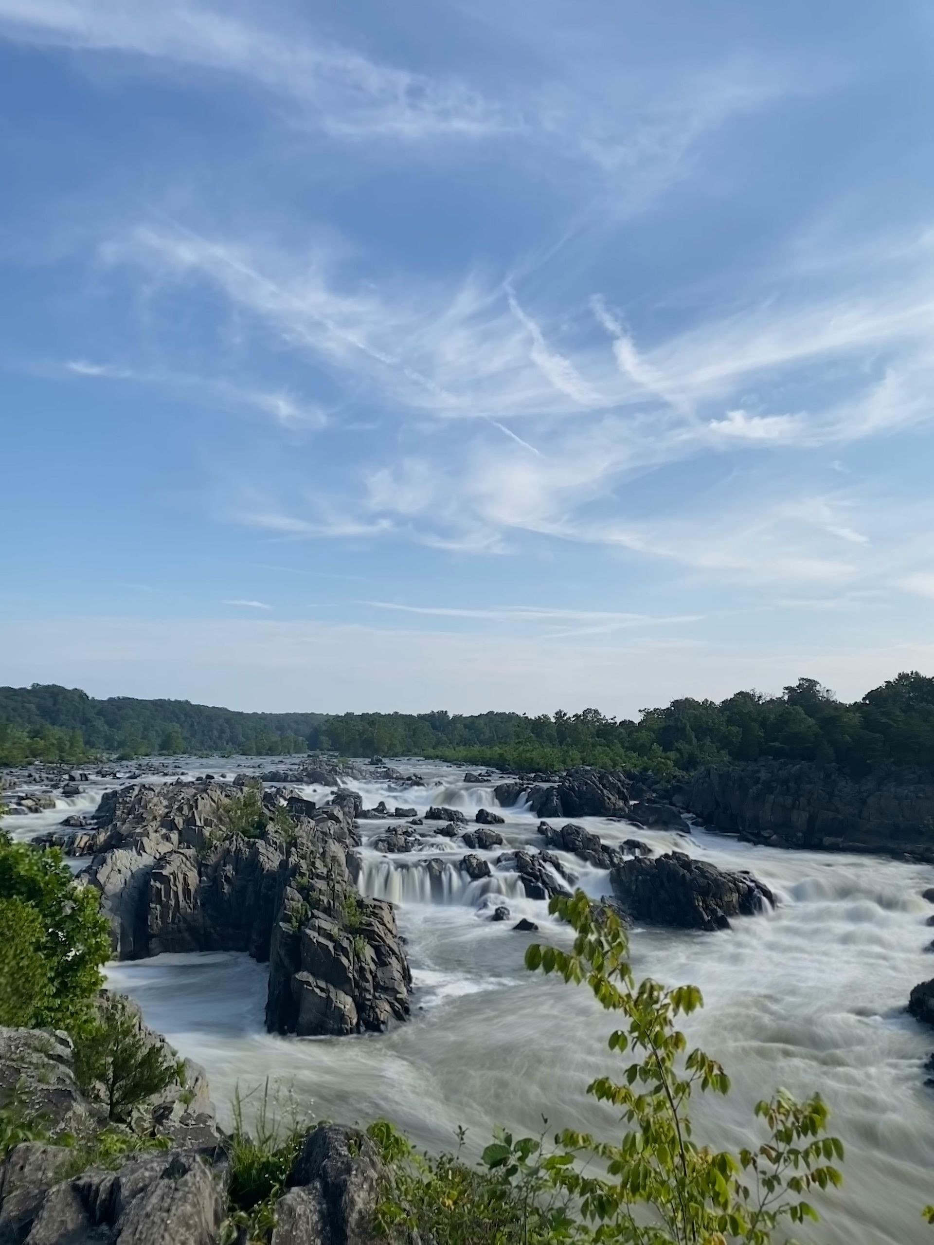 Houses nestled at the base of a tree-covered mountain in autumn. A road runs beside the houses under a blue sky.