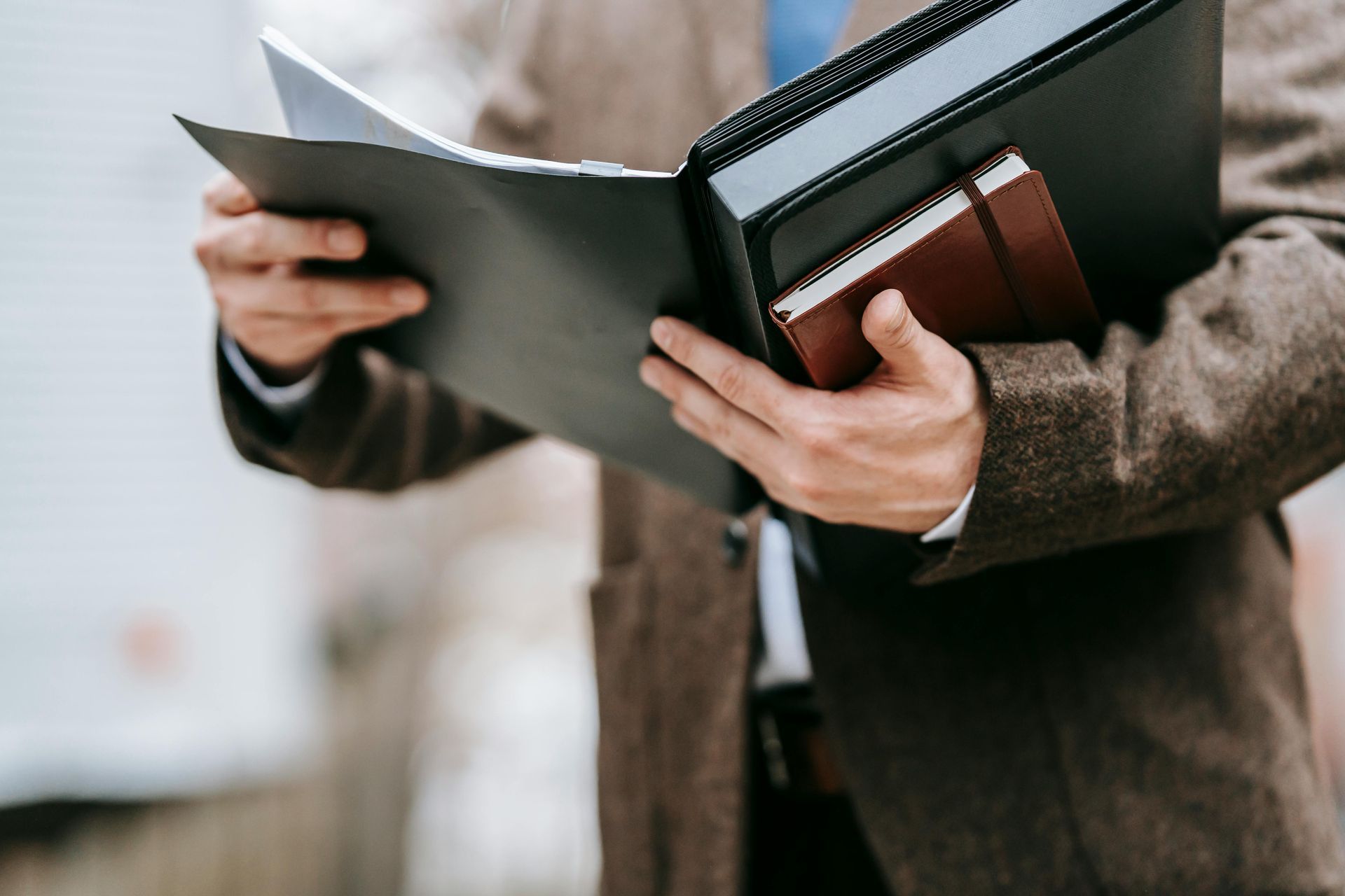 Person holding an open black binder with a laptop in a brown jacket