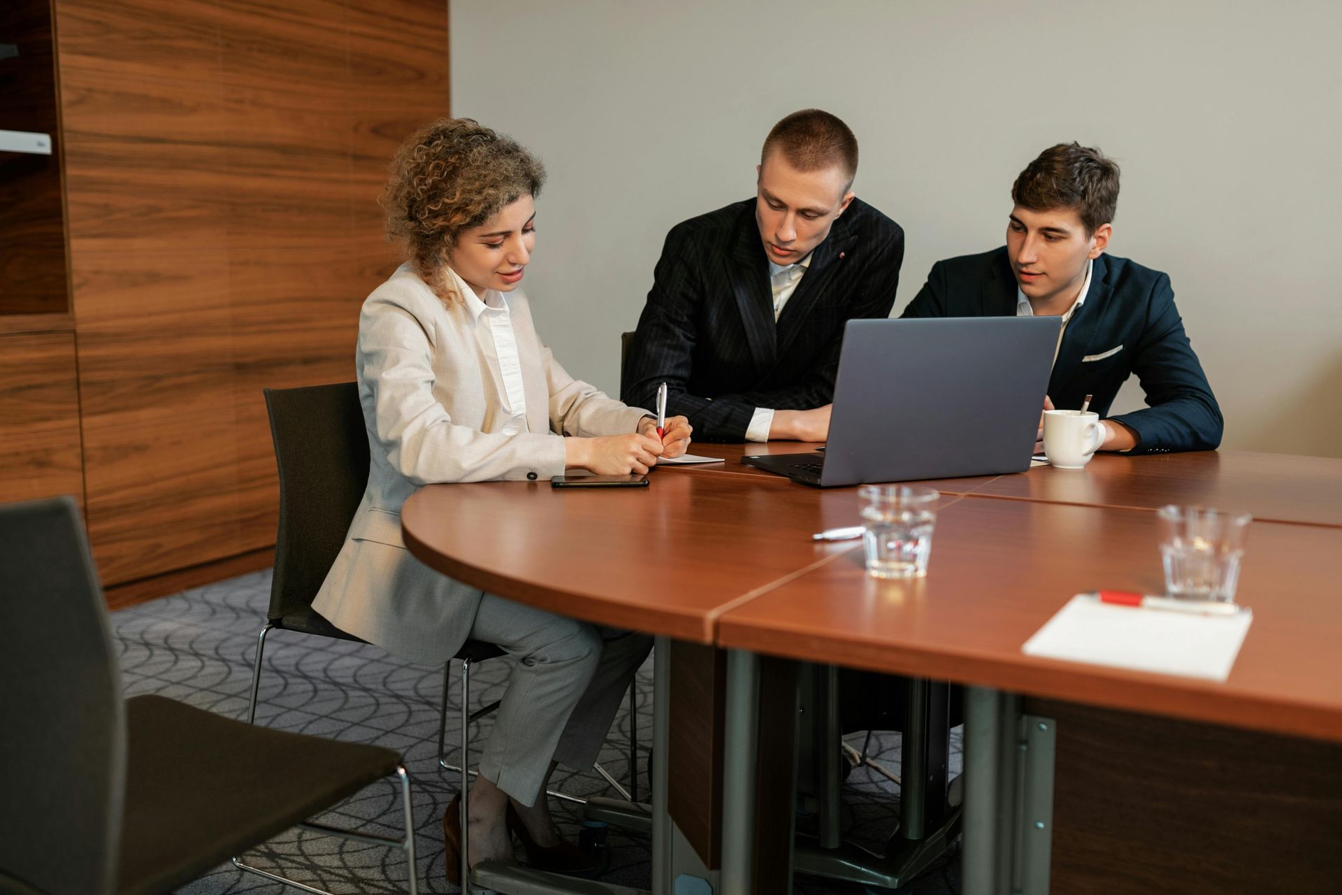 Three colleagues discussing a laptop at a conference table in a meeting room