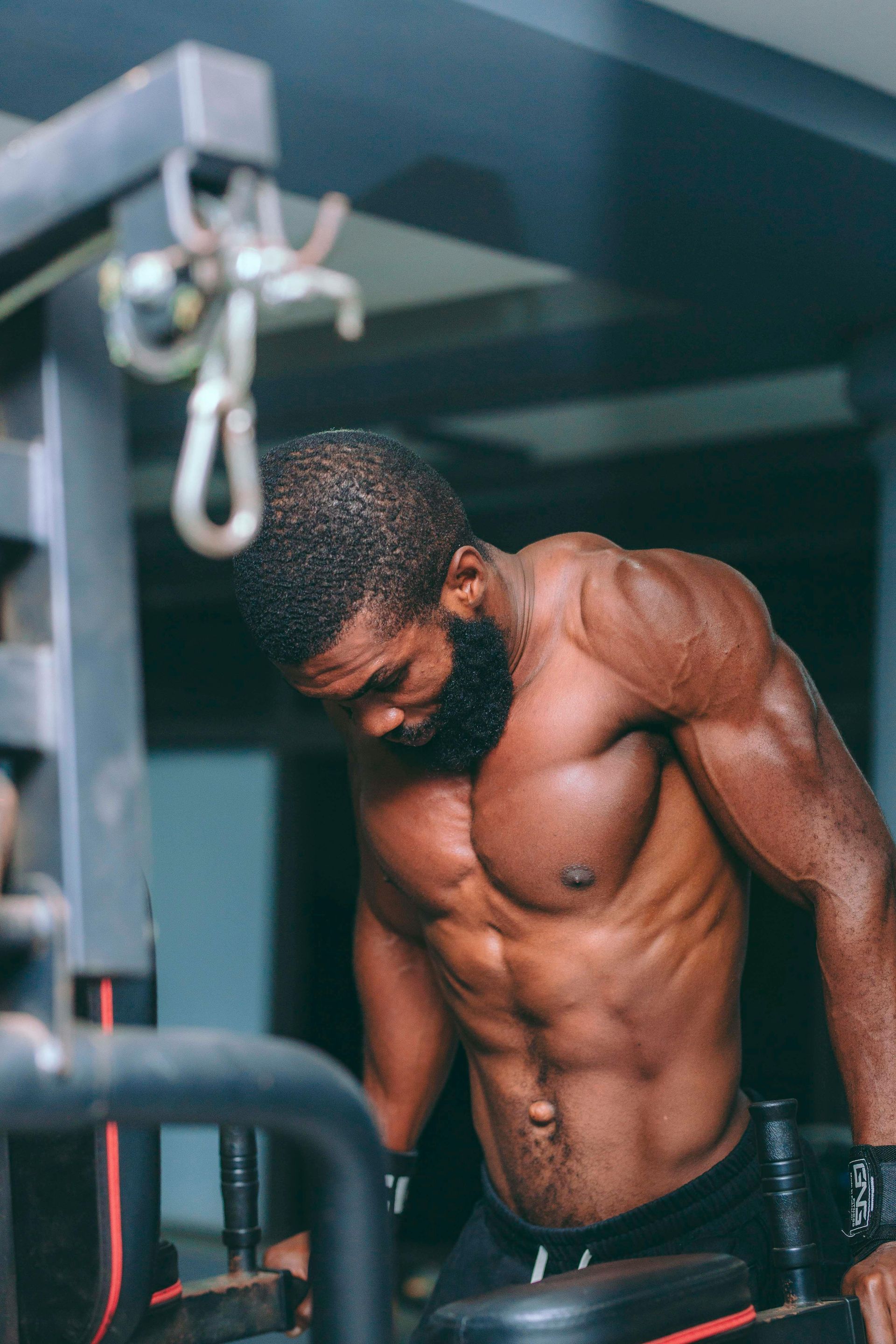 Muscular Black man at gym, gripping dip bars, intensely focused, with chiseled torso and arm muscles.