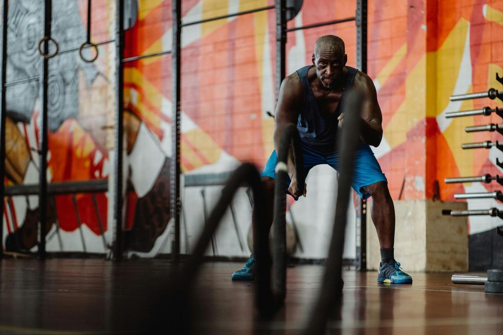 Man using battle ropes in a gym with colorful mural, blue shorts, and determined expression.