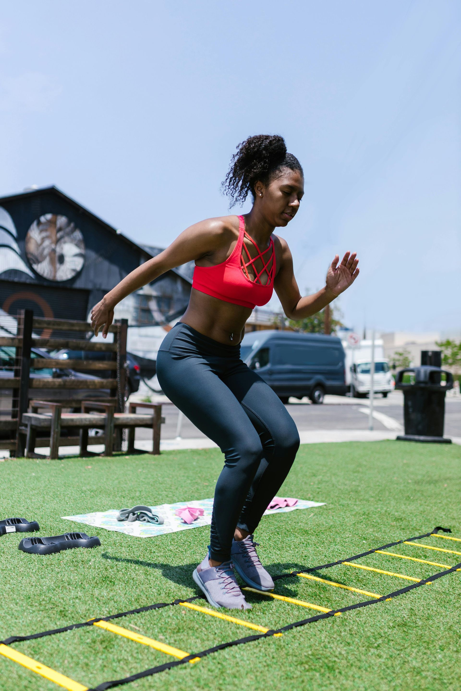 Woman in red sports bra and leggings doing ladder drills on outdoor turf.
