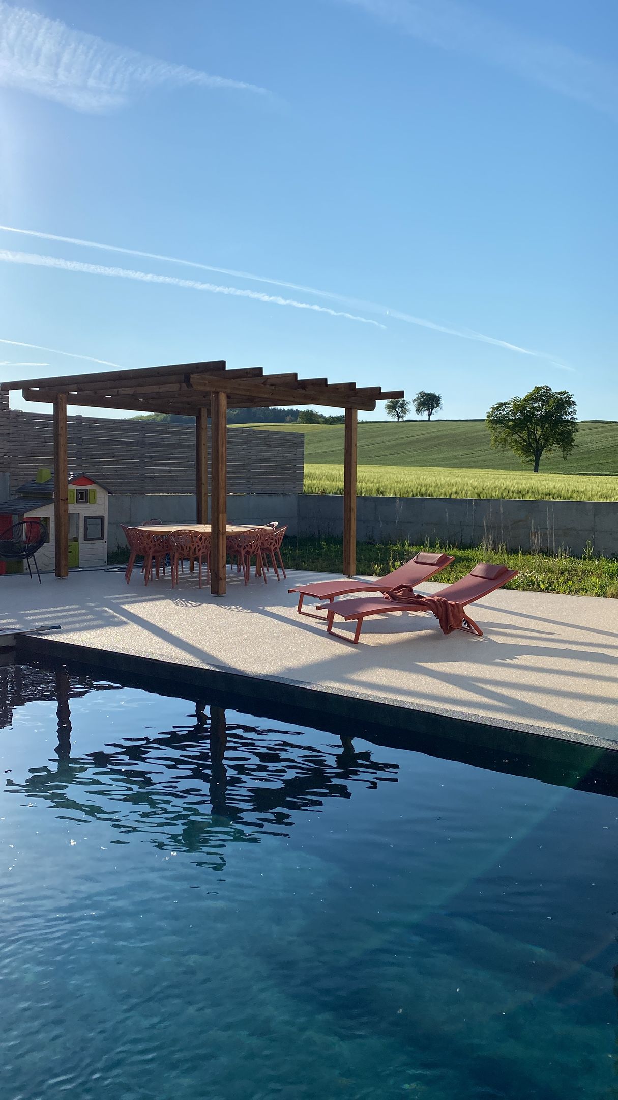 Une piscine avec une pergola et des chaises à côté.