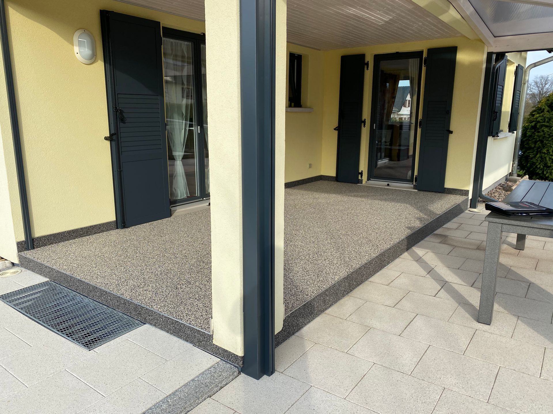 Une maison jaune avec des volets noirs et un patio