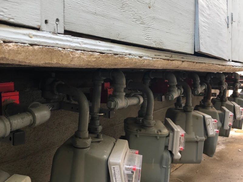 Gas meters attached to the side of a building, with multiple pipes and shutoff valves visible.
