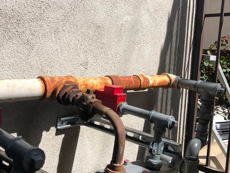 Rusty pipes and valves against a stucco wall.