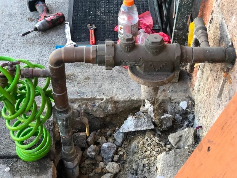 Plumbing pipes with tools, including a wrench and impact driver, on a concrete surface.