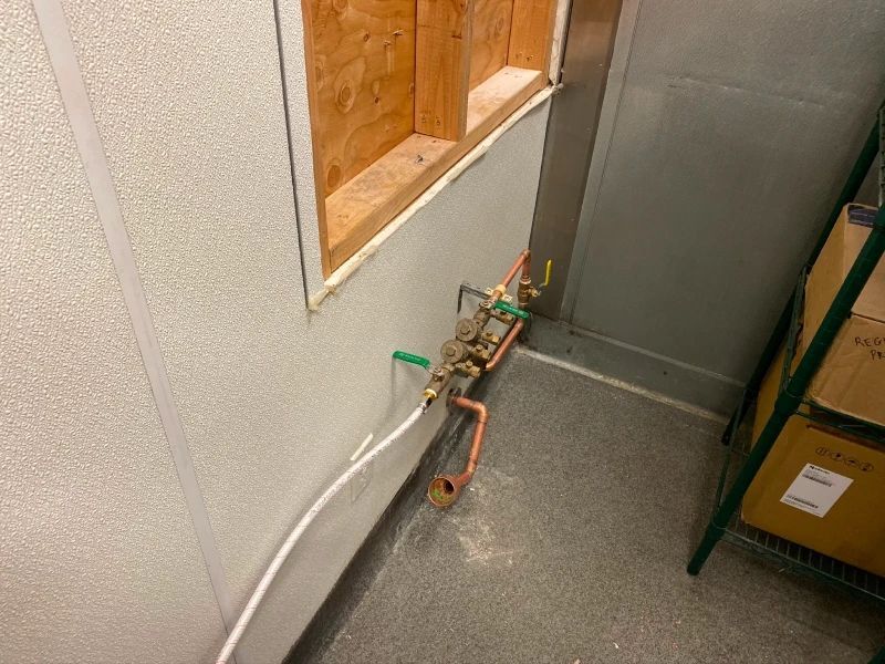 Copper pipes and valves against a textured white wall, below a wooden framed opening.