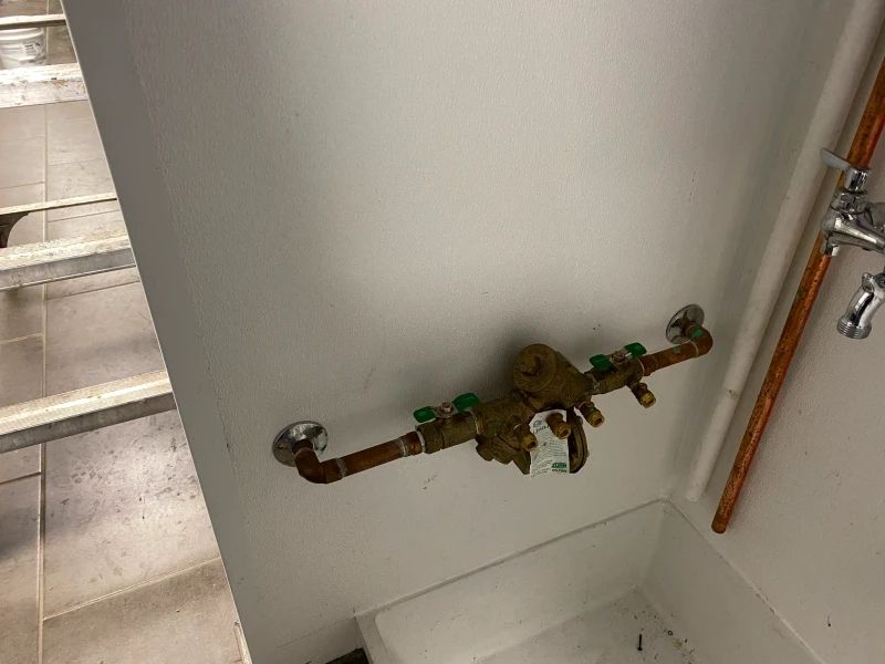Copper pipes and backflow preventer on a white wall above a utility sink.