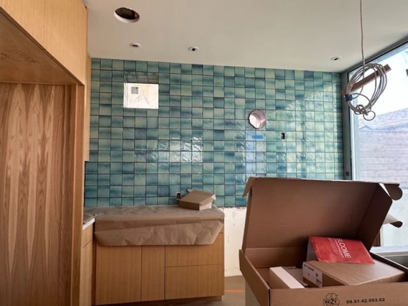 Kitchen under construction, blue tile backsplash, wooden cabinets, cardboard boxes, and unfinished fixtures.