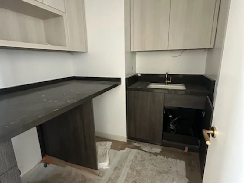 A small room with a sink, countertop, and cabinets. Dark gray and light wood tones.