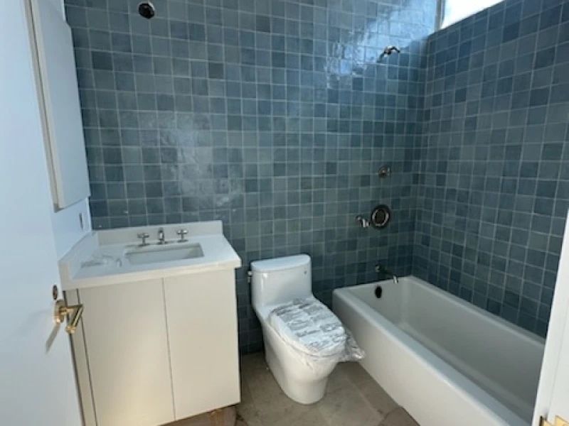 Bathroom with blue tiled walls, white vanity, toilet, and bathtub.