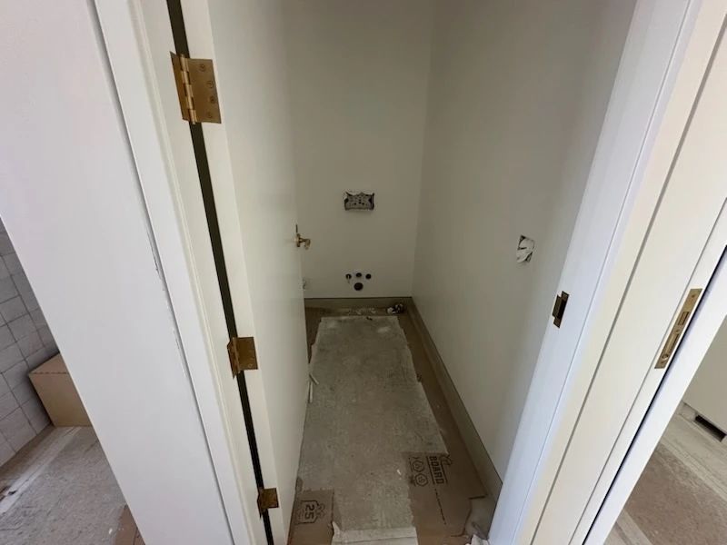 A narrow, white-painted utility closet with visible plumbing fixtures and electrical outlets on the back wall.
