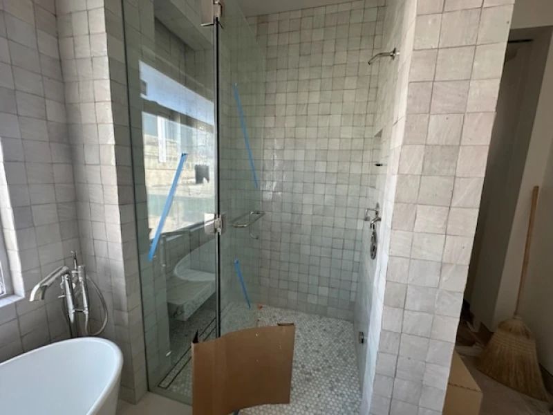 Bathroom with glass shower, white tiled walls, and a white bathtub.