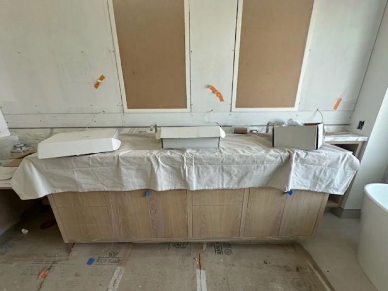 Bathroom renovation: Wooden tub covered with a tarp, materials on top. Wall has cardboard and tape.
